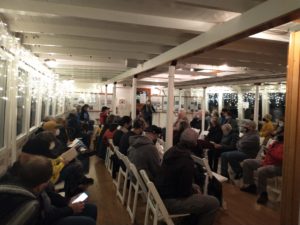 People sitting on chairs singing inside a historic ship